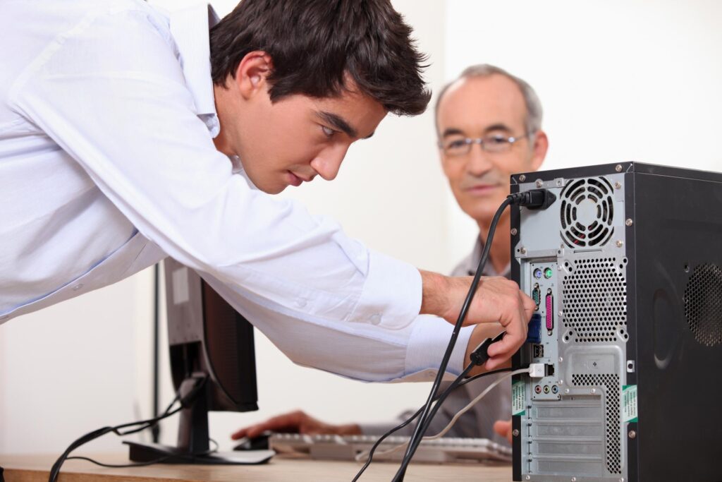 a man working on a computer next to another man